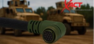 A close-up of a green military-grade electrical connector cable, with armored vehicles blurred in the background and the XACT company logo in the top right corner.